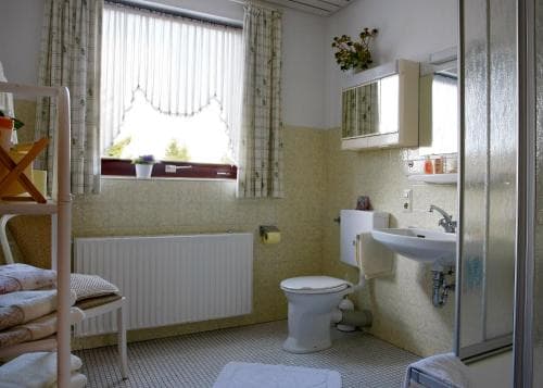 A cozy, vintage-style bathroom with pastel yellow walls, a window with lace curtains, and neatly arranged toiletries creates a warm and inviting atmosphere, perfect for travelers seeking a quaint and comfortable stay.