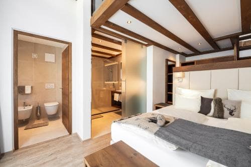 A cozy bedroom with wooden beams, a neatly made bed adorned with decorative pillows, and an open bathroom featuring modern fixtures, ideal for travelers seeking comfort in boutique accommodations.