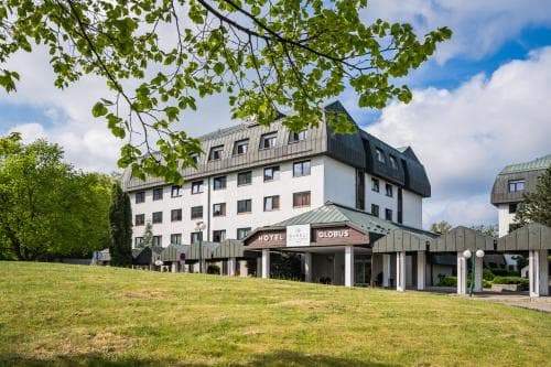 A serene hotel surrounded by lush greenery under a partly cloudy sky, featuring modern architecture with a prominent sign, ideal for travelers seeking a tranquil retreat in a natural setting.