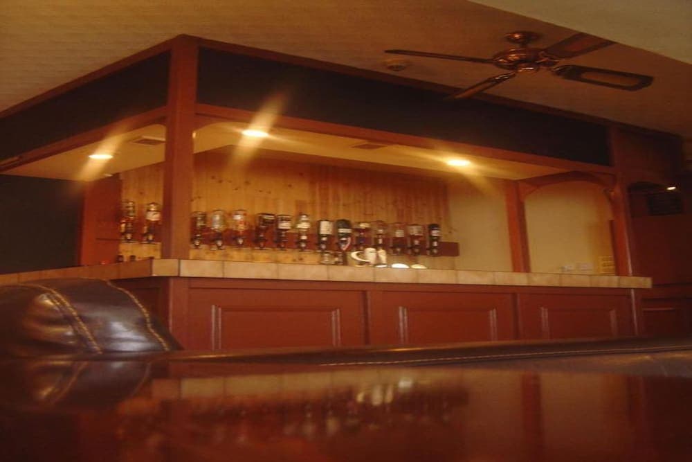 A cozy bar with wooden decor, shelves lined with bottles, and a leather booth invites travelers seeking a warm and intimate atmosphere for relaxation or socializing.