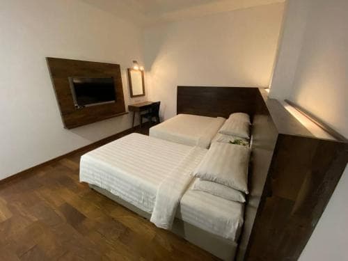 A cozy hotel room features two neatly made beds with white linens, a mounted TV, and warm lighting, creating an inviting atmosphere ideal for travelers seeking comfort and relaxation.