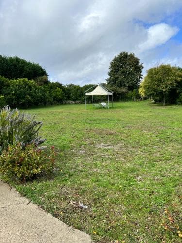A serene park scene features a grassy field bordered by lush greenery, a small white gazebo, and a paved path, ideal for a peaceful outdoor retreat or picnic spot.