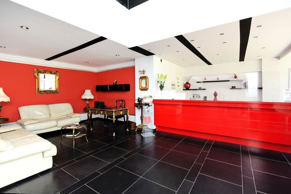 A vibrant hotel lobby features bold red walls, sleek black tiled floors, white leather seating, and modern decor, creating an inviting atmosphere ideal for travelers seeking a stylish accommodation experience.