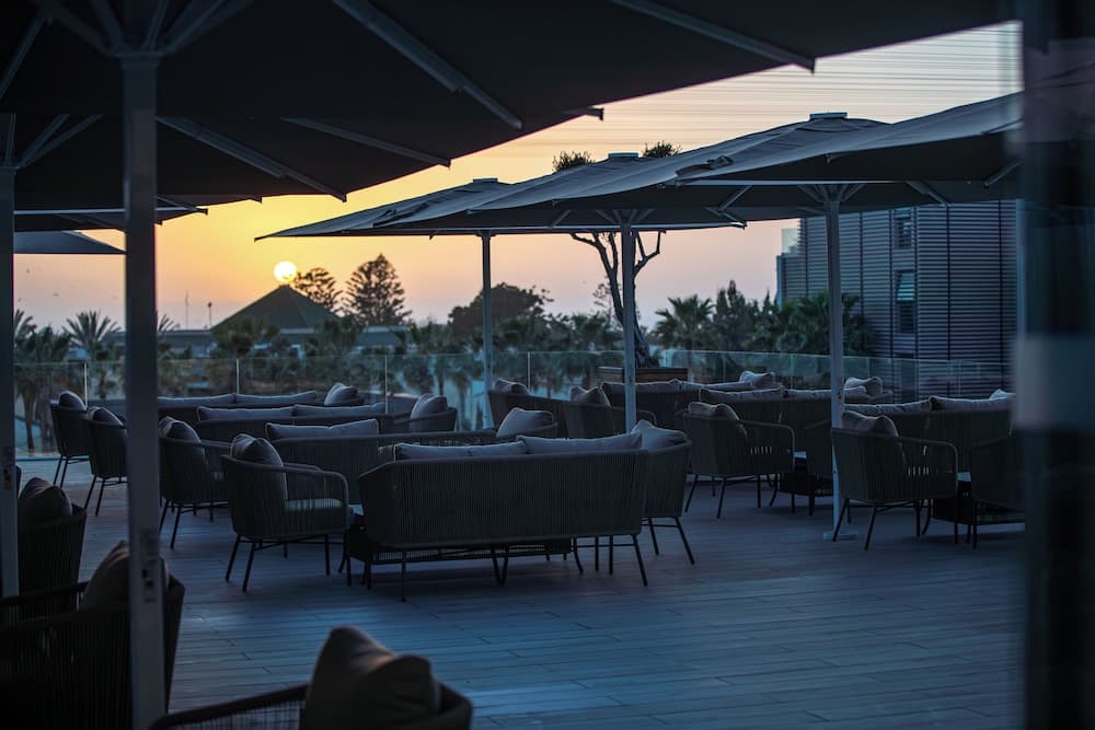 A serene rooftop lounge at sunset features modern seating under large umbrellas, ideal for travelers seeking relaxation and picturesque views.