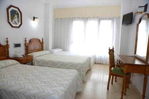 A cozy hotel room features two neatly made beds, wooden furniture, and soft natural light filtering through sheer curtains, ideal for travelers seeking comfort and relaxation.