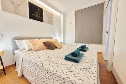 A cozy bedroom with a neatly made bed adorned with patterned bedding, soft pillows, and folded towels, set against a minimalist backdrop featuring wall art of deer and birds, ideal for travelers seeking a serene and stylish accommodation.
