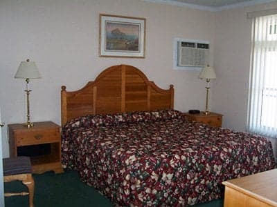 A cozy hotel room features a neatly made bed with a floral comforter, wooden furnishings, and soft lighting, creating a welcoming atmosphere ideal for travelers seeking rest and relaxation.