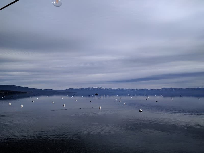 A serene lakeside view with calm waters dotted by white buoys under an overcast sky, ideal for tranquil vacations near Lake Tahoe.
