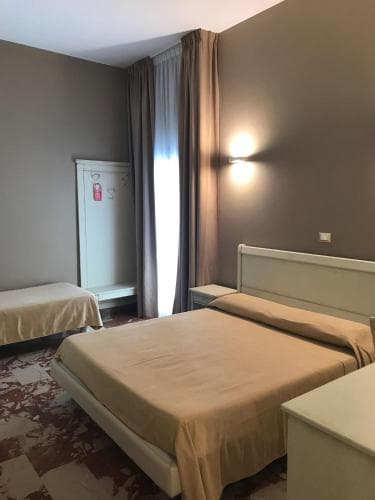 A cozy hotel room features a neatly made bed with beige linens, a patterned carpet, and soft lighting from wall-mounted lamps, ideal for travelers seeking comfort and relaxation.