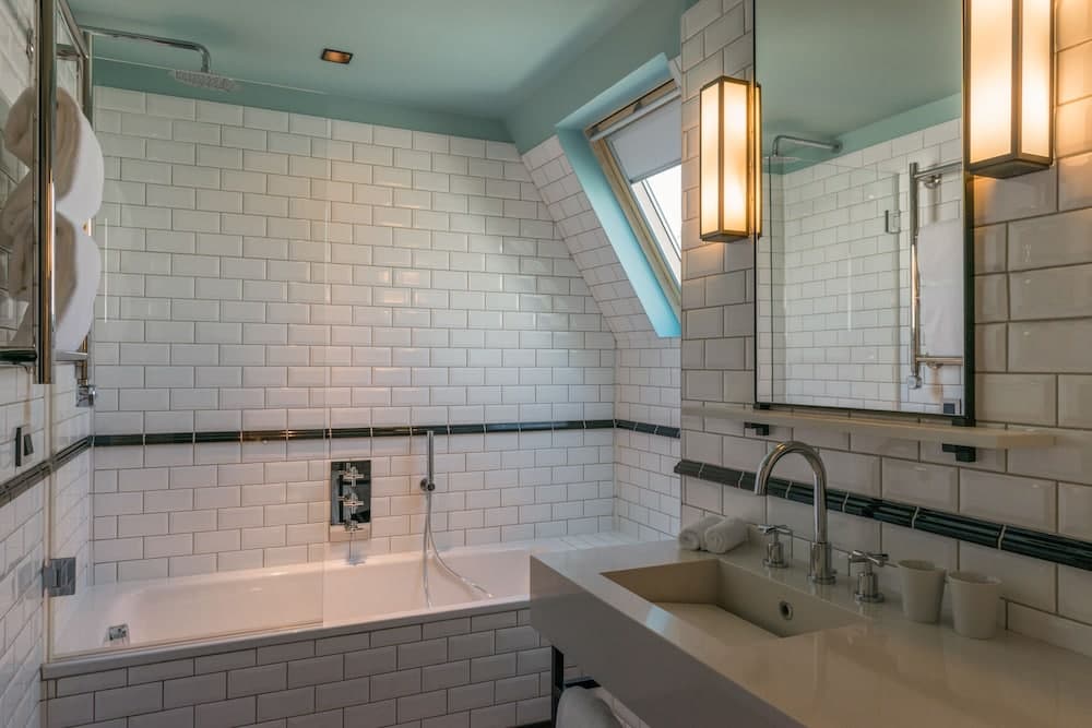 A serene hotel bathroom features white subway tiles, a modern bathtub, a sleek sink, and warm lighting, creating an inviting atmosphere ideal for relaxation during travel.