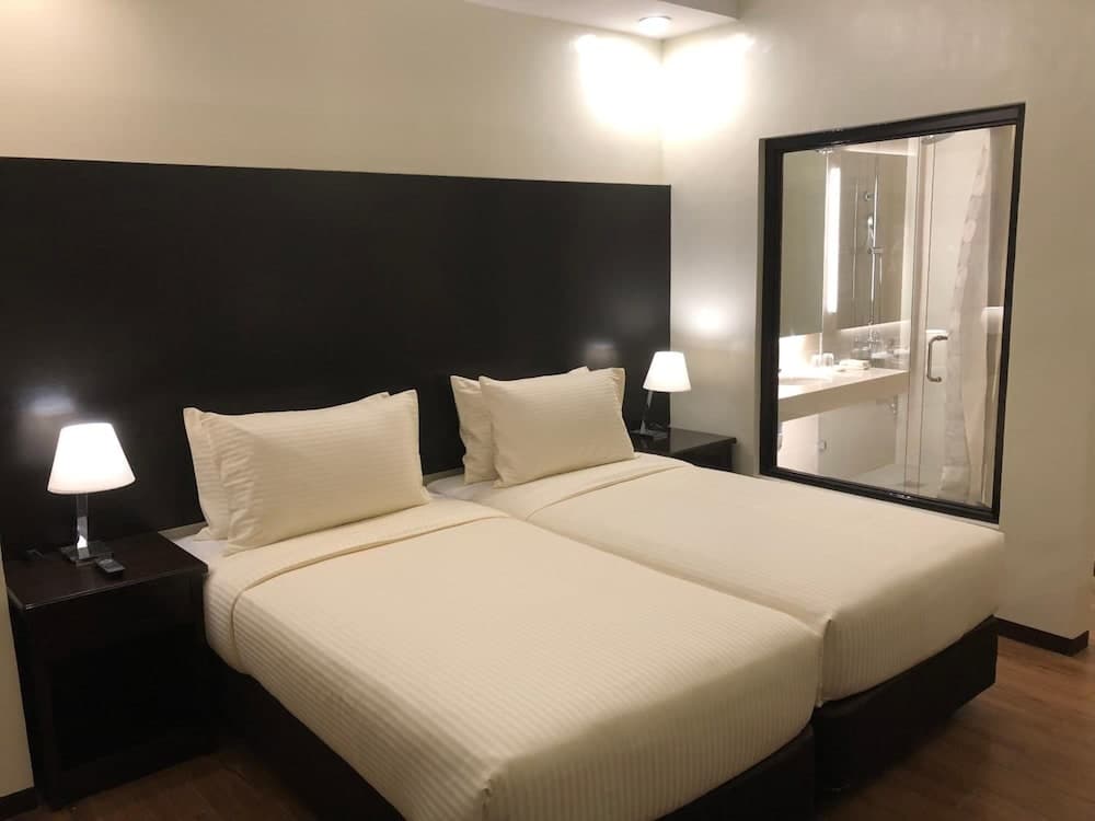 A cozy hotel room features two neatly made beds with white linens, black bedside tables with lamps, and a large mirror reflecting the bathroom, ideal for travelers seeking comfort and convenience.