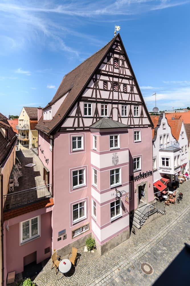 A charming pink half-timbered building stands out on a cobblestone street in a quaint European town, perfect for travelers seeking picturesque architecture and a serene atmosphere.