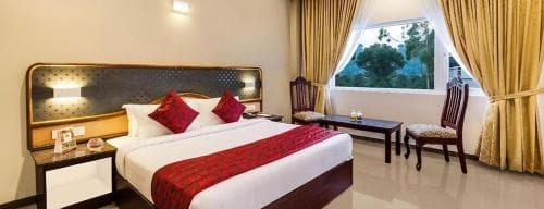 A cozy hotel room with a neatly made bed adorned in red accents, wooden furniture, and a bright window view, evokes a warm and inviting atmosphere ideal for travelers seeking comfort and relaxation.