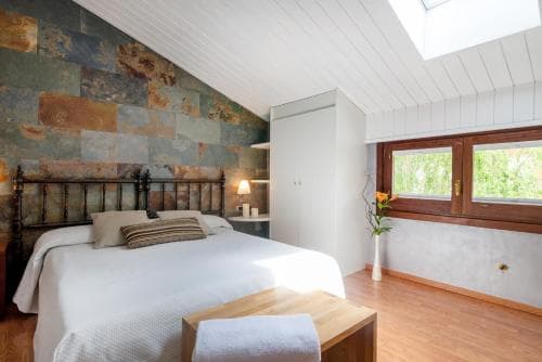 A cozy attic bedroom with a stone accent wall, wooden furnishings, and natural light from a skylight and window, ideal for a serene getaway in a rustic retreat.