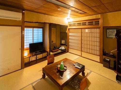 A cozy traditional Japanese room with tatami flooring, wooden sliding doors, and a low table set for tea, ideal for travelers seeking authentic cultural accommodation.