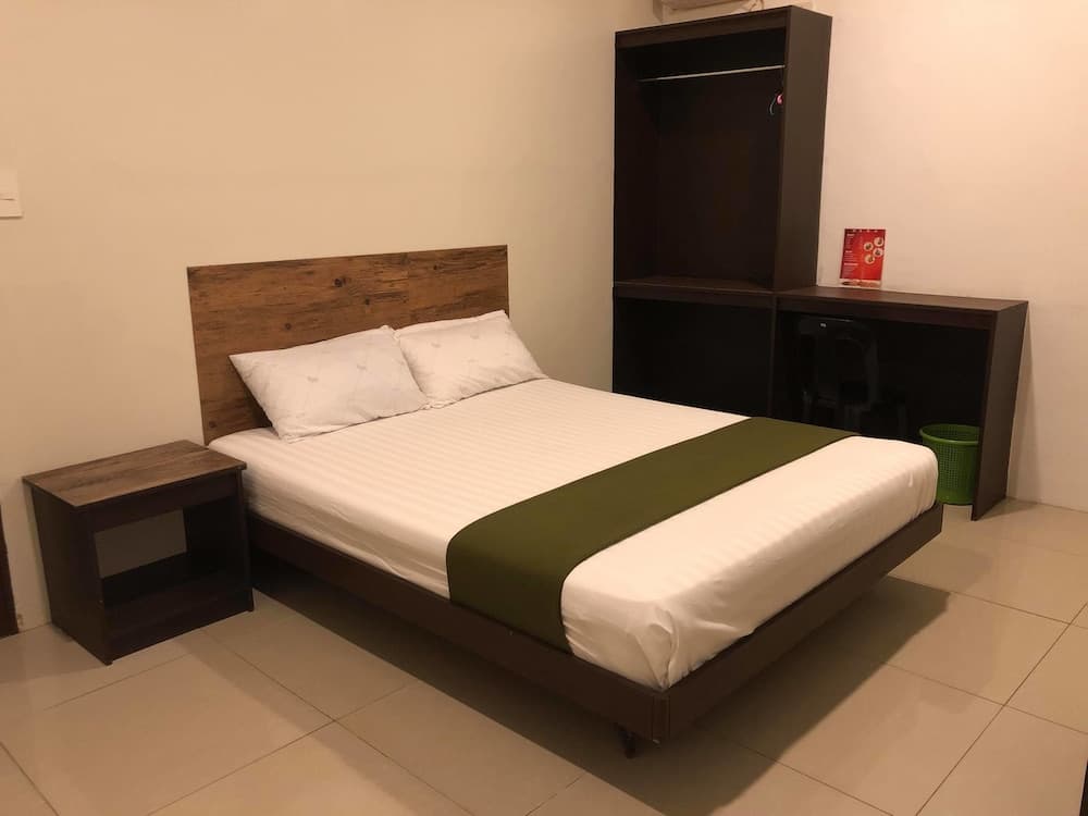 A cozy minimalist bedroom with a neatly made bed adorned with a green throw, wooden furniture, and tiled flooring, ideal for travelers seeking simplicity and comfort.