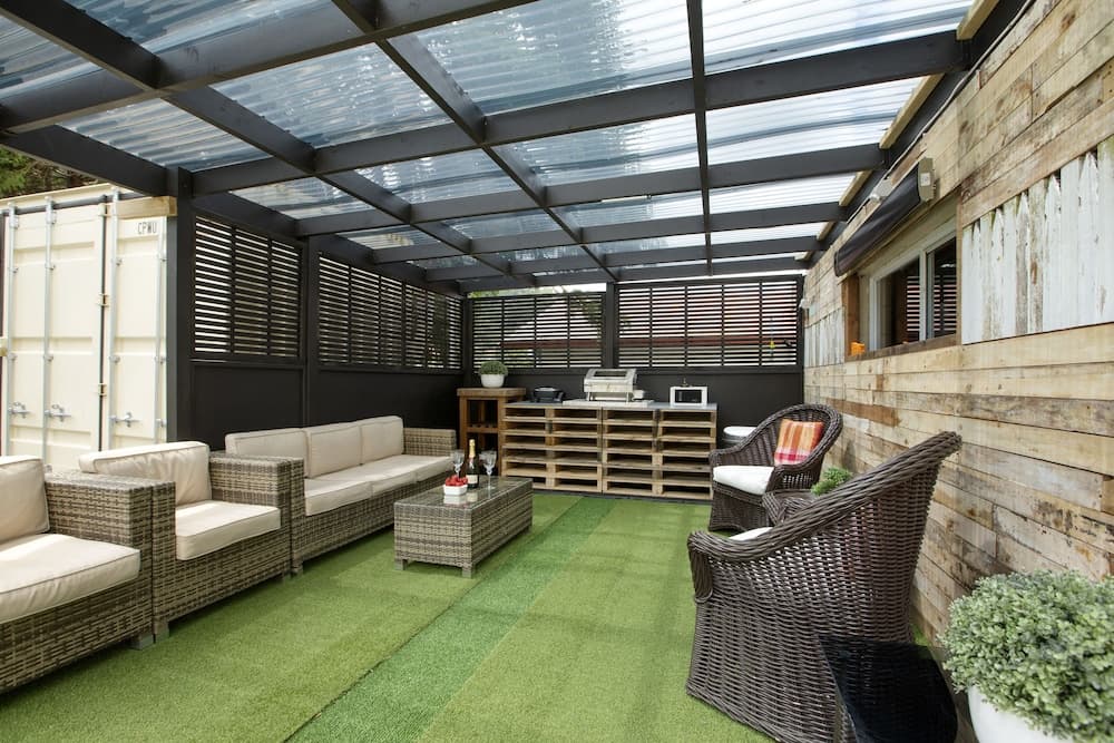 A cozy outdoor patio with artificial turf flooring, wicker furniture, and a translucent roof creates a serene retreat perfect for relaxation or hosting intimate gatherings.