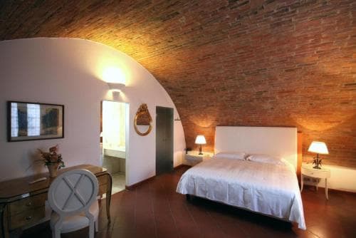 A cozy bedroom with a brick-vaulted ceiling exudes rustic charm, featuring a neatly made bed, warm lighting, and classic furnishings, ideal for travelers seeking a unique and intimate accommodation experience.