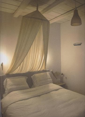 A cozy bedroom with a canopy-draped bed under a wooden ceiling exudes a serene ambiance, ideal for travelers seeking relaxation in rustic accommodations.