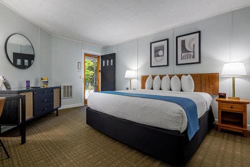 A cozy hotel room features a neatly made bed with white pillows, framed artwork on the walls, and a desk area, creating a welcoming atmosphere ideal for travelers seeking comfort and relaxation.