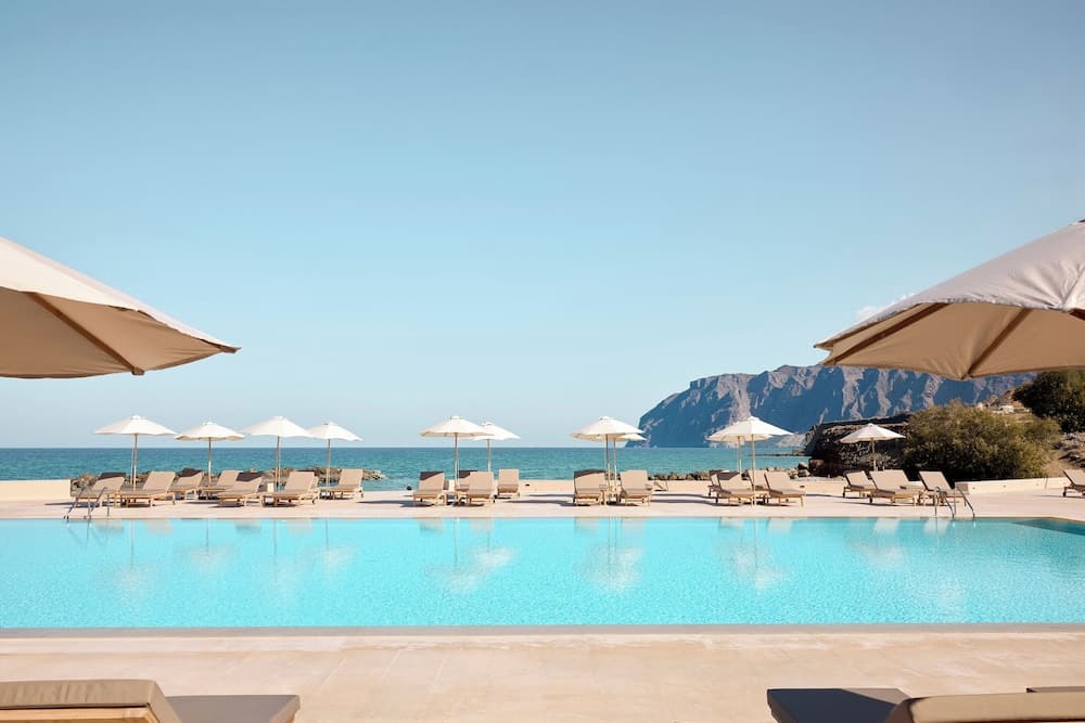 A serene luxury resort poolside scene with lounge chairs, umbrellas, and a stunning view of turquoise waters and rugged mountains, ideal for relaxation and vacation photography.