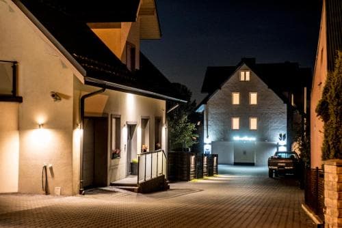 A cozy European village street at night, illuminated by warm outdoor lights, features quaint houses with wooden accents, creating an inviting atmosphere perfect for a serene evening stroll or a tranquil getaway.
