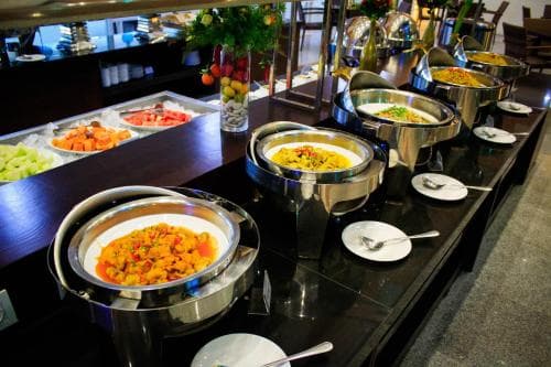 A vibrant hotel buffet scene showcases an array of colorful dishes in stainless steel containers, inviting travelers to indulge in a hearty meal during their stay.