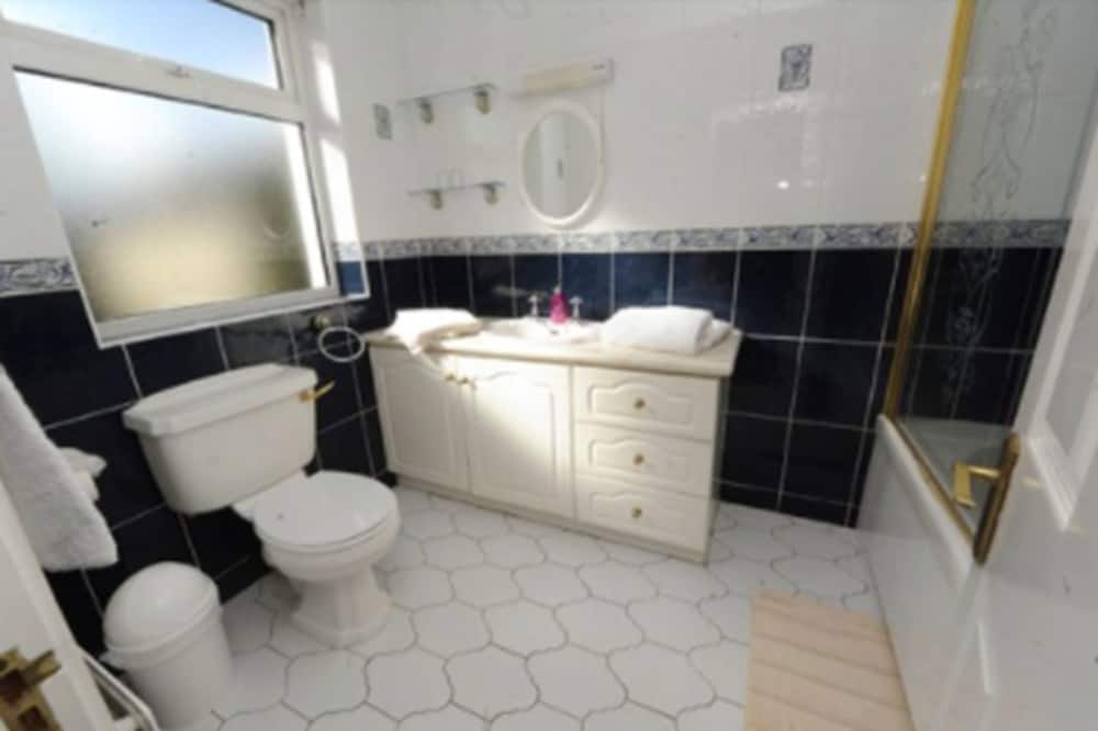 A cozy bathroom with white hexagonal tiles, black wall tiles, a white vanity with towels, and a frosted window offers a serene retreat for travelers seeking comfort and cleanliness.