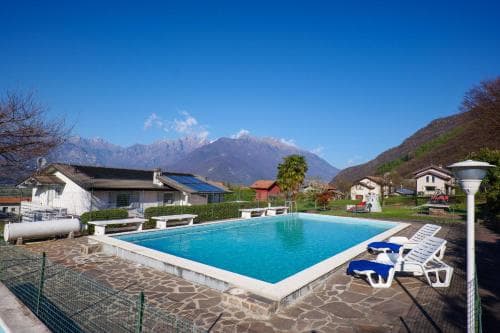 A serene mountain retreat features a sparkling pool surrounded by lounge chairs, set against a backdrop of lush hills and clear blue skies, ideal for a relaxing vacation getaway.