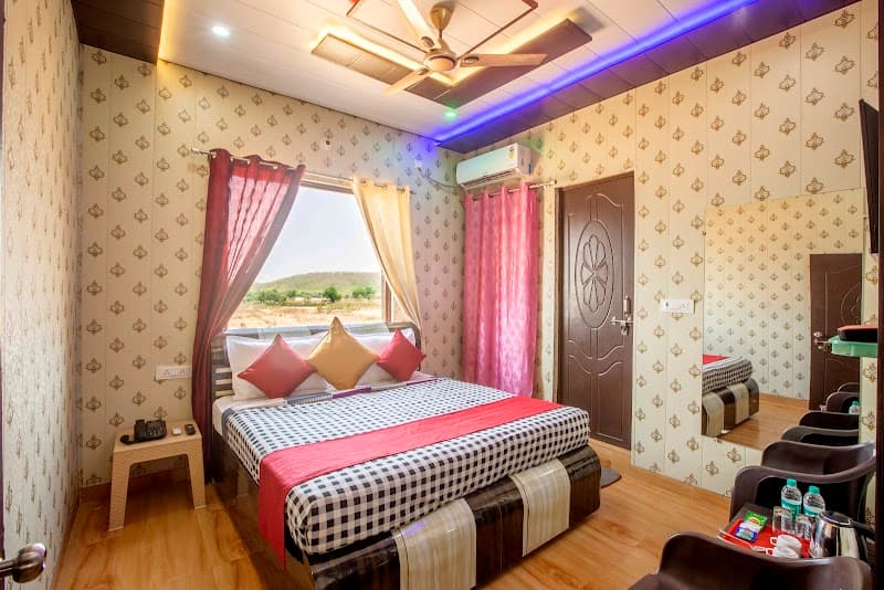 A cozy hotel room at Jhansi Castle Inn features patterned wallpaper, a neatly made bed with colorful pillows, a scenic view through the window, and modern amenities, ideal for travelers seeking comfort in Jhansi, Uttar Pradesh.