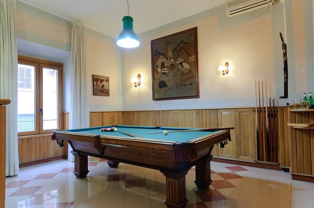 A cozy indoor recreation room features a classic pool table under warm lighting, adorned with wooden paneling, framed artwork, and a checkered floor, ideal for leisurely stays at a boutique hotel or vacation rental.