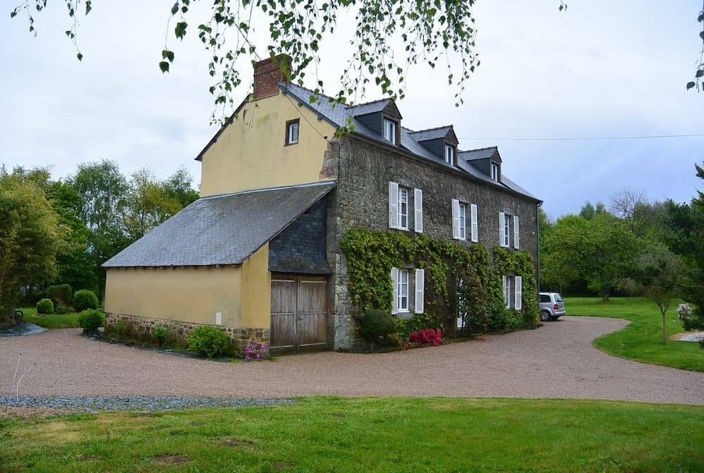 A serene countryside retreat features a charming stone and plaster house surrounded by lush greenery, ideal for a peaceful rural getaway.