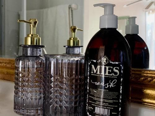 A cozy bathroom vanity features elegant glass dispensers and a luxurious MIES wash bottle, creating an inviting atmosphere ideal for travelers seeking comfort and style in their accommodations.