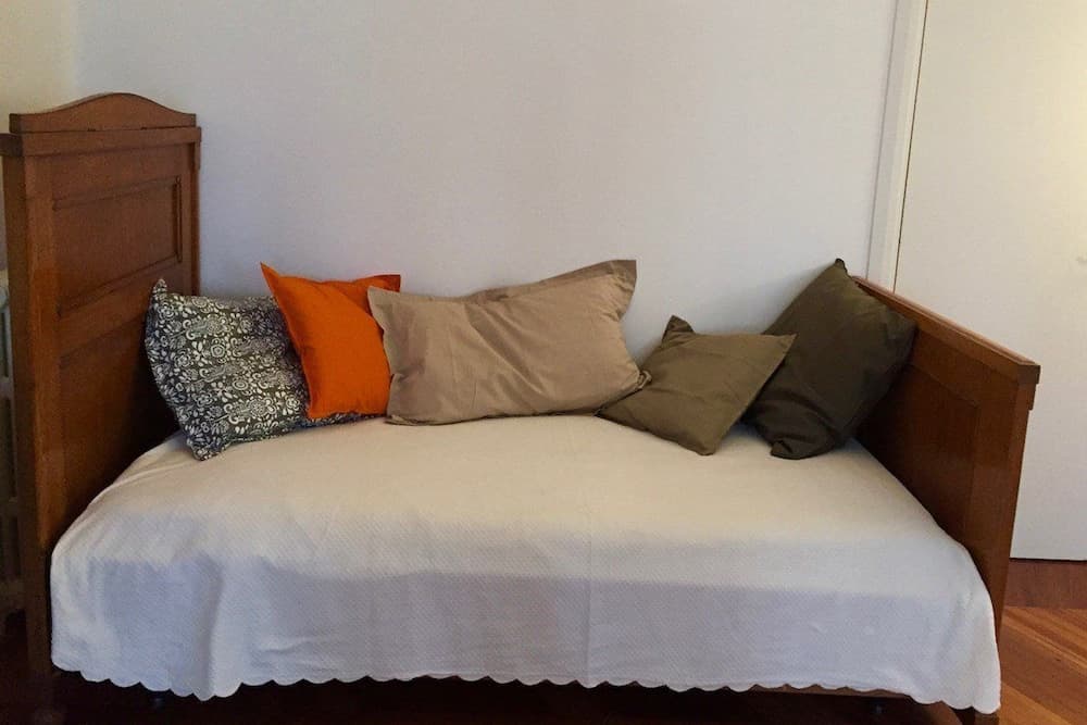 A cozy daybed adorned with colorful pillows invites relaxation in a minimalist room, perfect for travelers seeking comfort in a simple yet stylish accommodation.