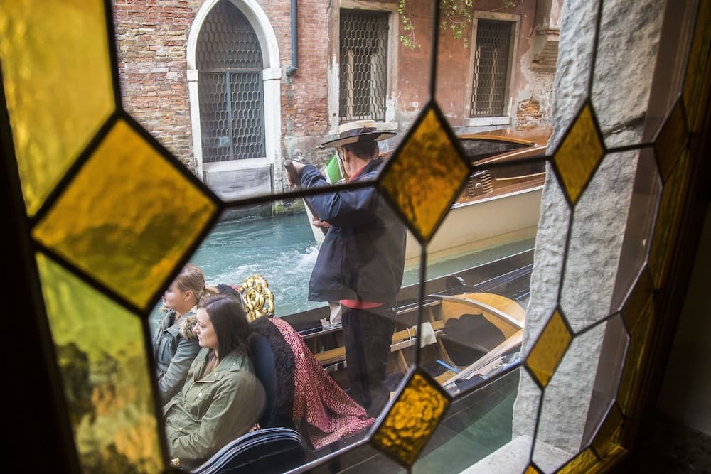 A serene gondola ride through Venice's narrow canals is captured through a stained-glass window, showcasing the city's historic charm and offering a romantic travel experience.