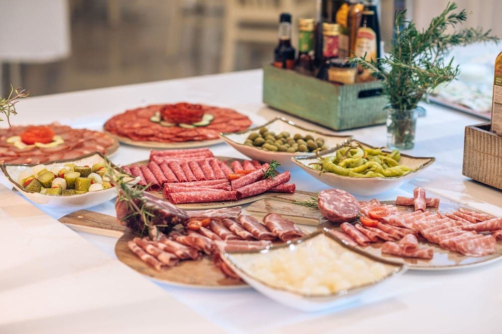 A vibrant charcuterie spread featuring cured meats, olives, and pickled vegetables on a white tablecloth creates an inviting atmosphere perfect for a gourmet food tour or culinary workshop.