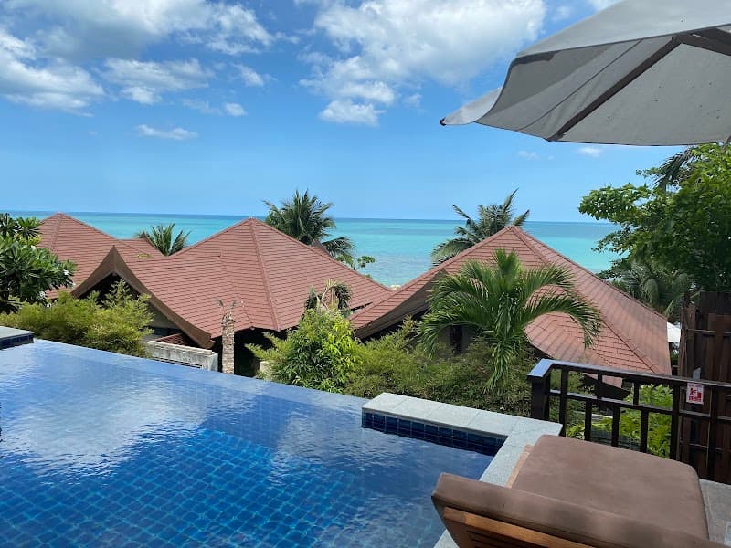 A serene tropical resort scene featuring lush greenery, red-roofed villas, and an infinity pool overlooking the turquoise sea under a bright blue sky, ideal for luxury beachfront relaxation in Koh Samui, Thailand.