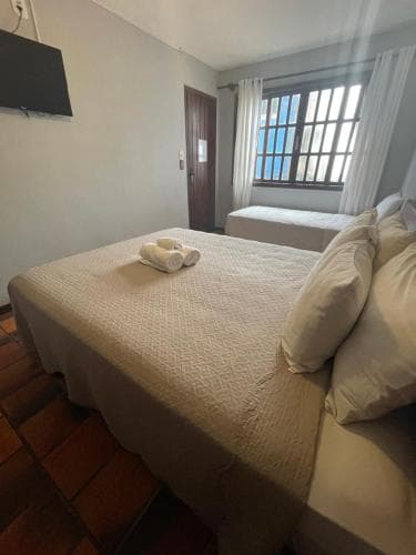 A cozy hotel room with neatly arranged beds, soft lighting from a window with white curtains, and a tiled floor, ideal for travelers seeking comfort and simplicity during their stay.