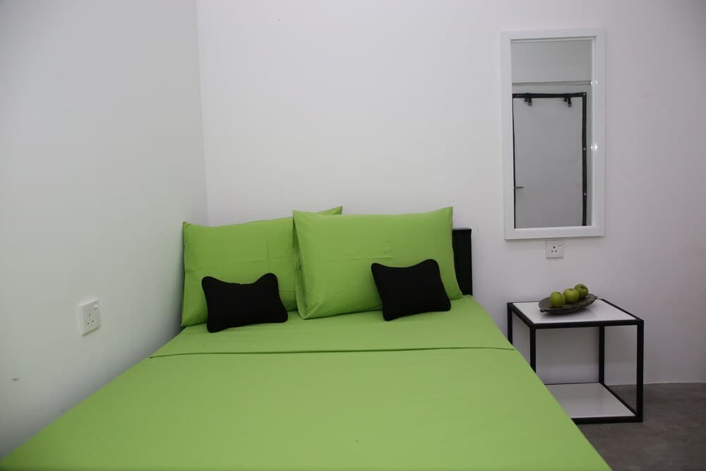 A minimalist bedroom with vibrant green bedding and black accents exudes a modern, cozy vibe, ideal for travelers seeking a clean and stylish accommodation option.