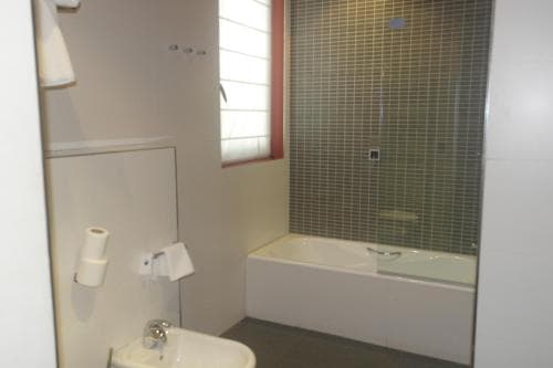 A modern bathroom with a tiled bathtub, frosted glass shower screen, and natural light from a window, ideal for travelers seeking clean and functional accommodations.