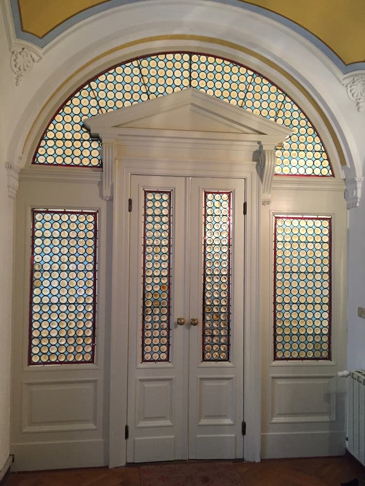An elegant interior hallway features ornate double doors framed by intricate stained glass windows, creating a sophisticated atmosphere ideal for heritage tourism and architectural appreciation.
