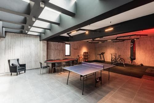 A modern indoor recreational space features a ping pong table, exercise equipment, and cozy seating under sleek lighting, ideal for travelers seeking a multifunctional leisure area in a boutique hotel or upscale residence.