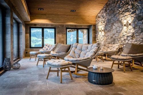 A cozy lounge area with rustic stone walls, wooden ceilings, and plush seating offers a serene retreat for travelers seeking relaxation in a mountain resort setting.