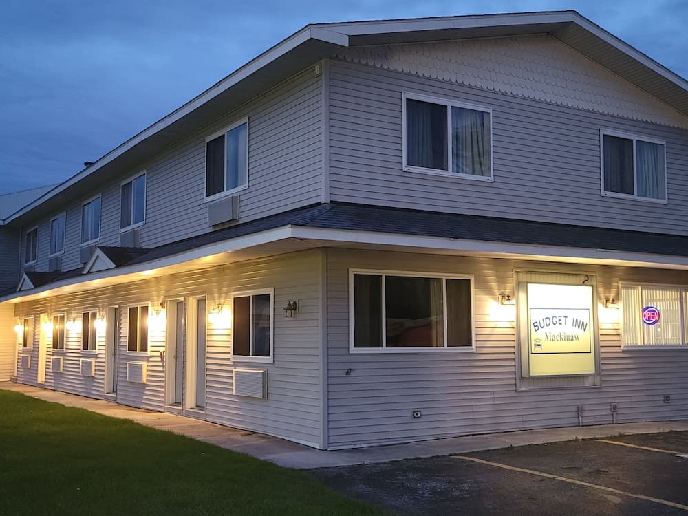 A cozy two-story Budget Inn illuminated by warm exterior lights at dusk, offering travelers a welcoming accommodation option in a quiet suburban setting.