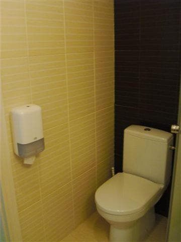 A compact restroom with yellow tiled walls, a white toilet, and a wall-mounted dispenser creates a functional and clean space ideal for travelers seeking basic facilities during their journey.
