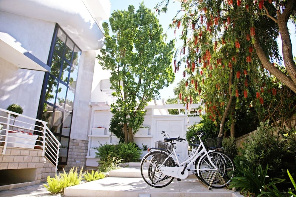 A serene courtyard with modern architecture, lush greenery, blooming trees, and parked bicycles offers a tranquil retreat ideal for leisurely stays and eco-friendly exploration.