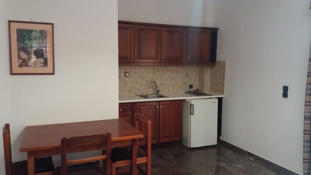 A cozy apartment kitchenette features wooden cabinets, a small dining table, and a compact refrigerator, ideal for travelers seeking a self-catering stay in an urban setting.