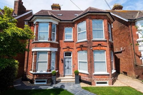 A charming red-brick Victorian terraced house with bay windows and lush greenery exudes a cozy suburban vibe, perfect for travelers seeking a quaint residential stay.
