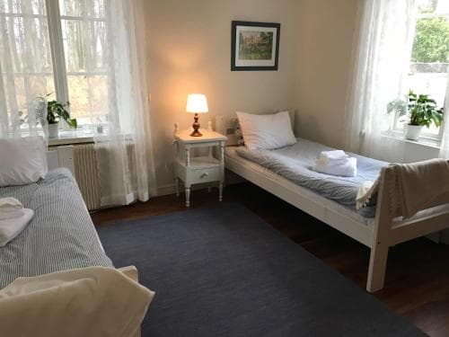 A cozy, well-lit bedroom with two single beds, soft furnishings, and large windows draped in sheer curtains creates a serene atmosphere ideal for travelers seeking a peaceful retreat.