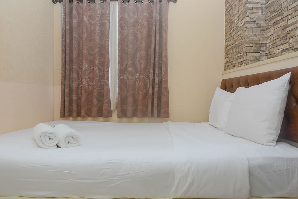 A cozy hotel room features a neatly made bed with white linens, rolled towels, a brown leather headboard, patterned curtains, and a stone accent wall, ideal for travelers seeking comfort and simplicity.